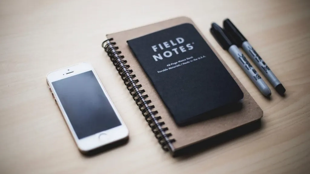 notepad, iphone, and two markers on a desk.